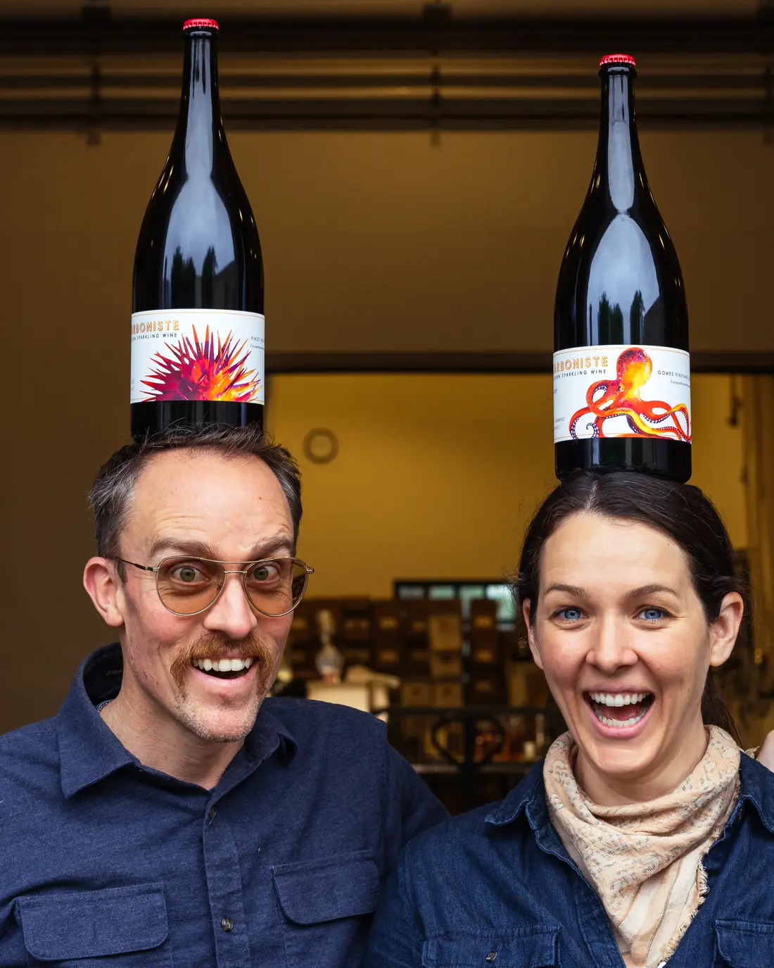 Carboniste founders Dan and Jacqueline Person balancing magnums of their sparkling wine on their heads in the cellar
